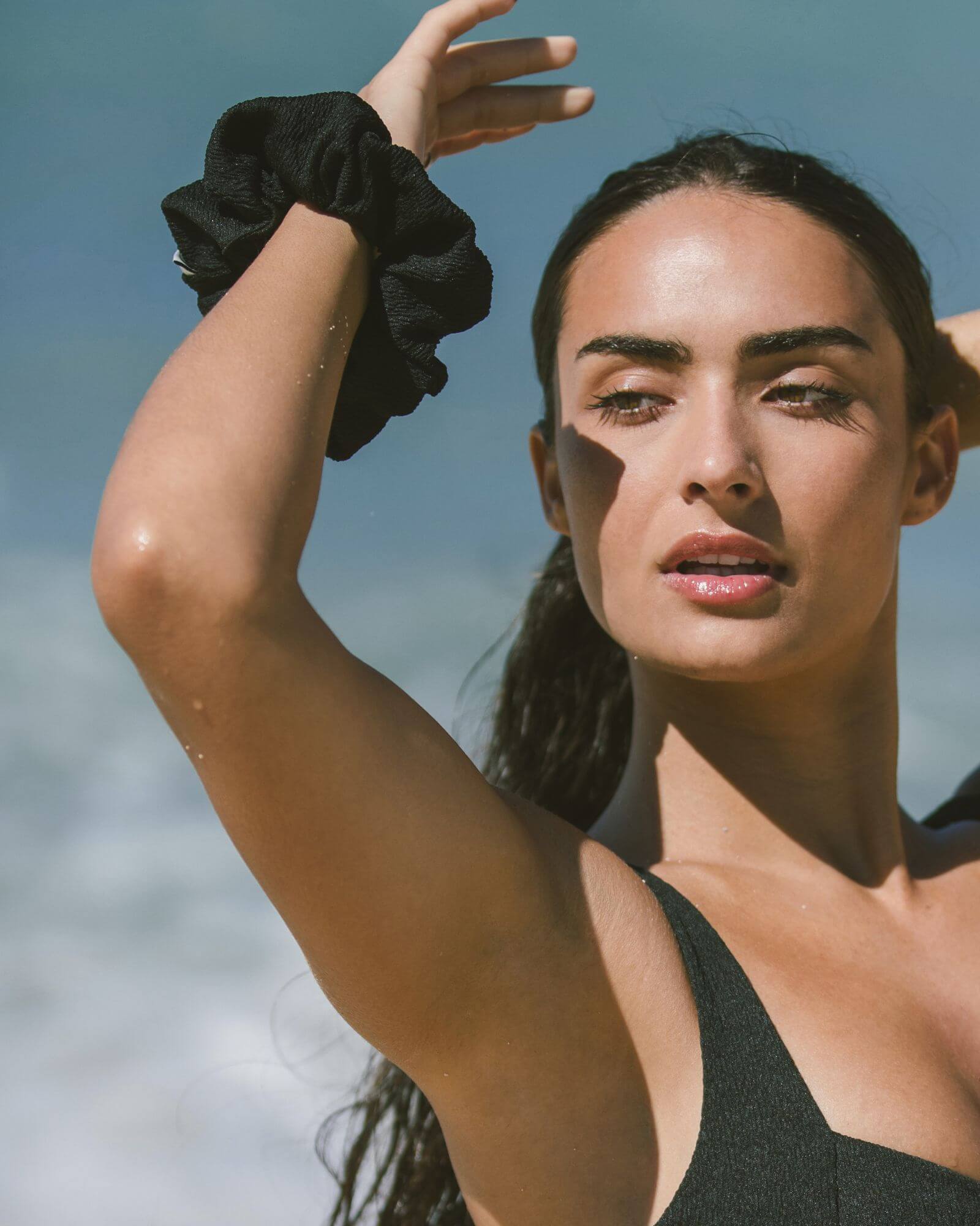 Beautiful girl is tying her hair with a black scrunchie on the beach.