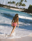 Beautiful girl walking by the ocean wearing a red checkered bikini and shorts.