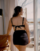 Pretty girl looking outside of a window while wearing a cute black rib bikini along with the matching sarong.