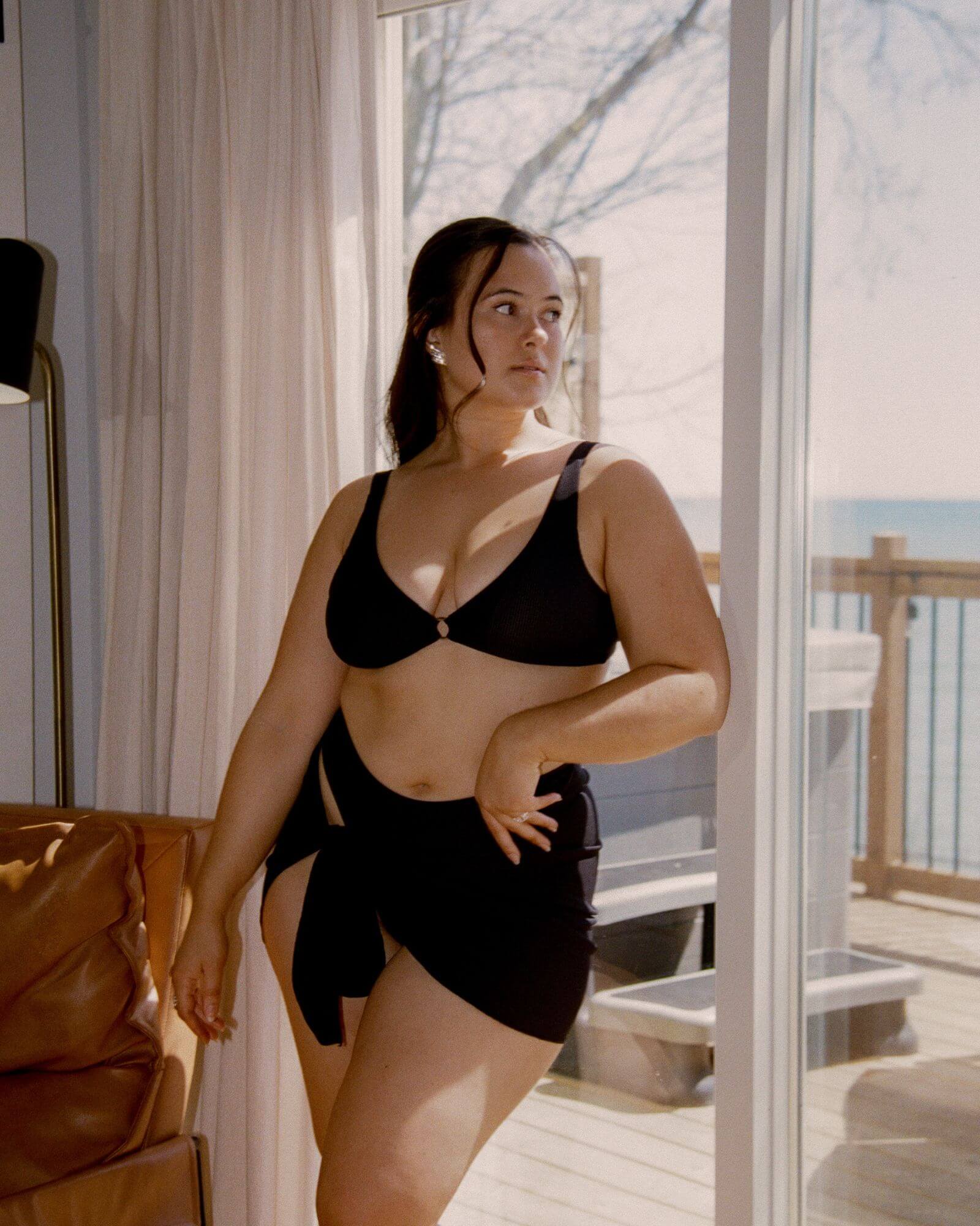 Pretty girl leaning against a window while wearing a cute black rib bikini along with the matching sarong.