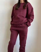 Close-up of a girl wearing a cute burgundy matching set with her hands in her pockets in front of a white background.