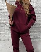 Front view of a girl holding a bouquet of flowers in front of a white brick wall wearing a cute burgundy matching set.