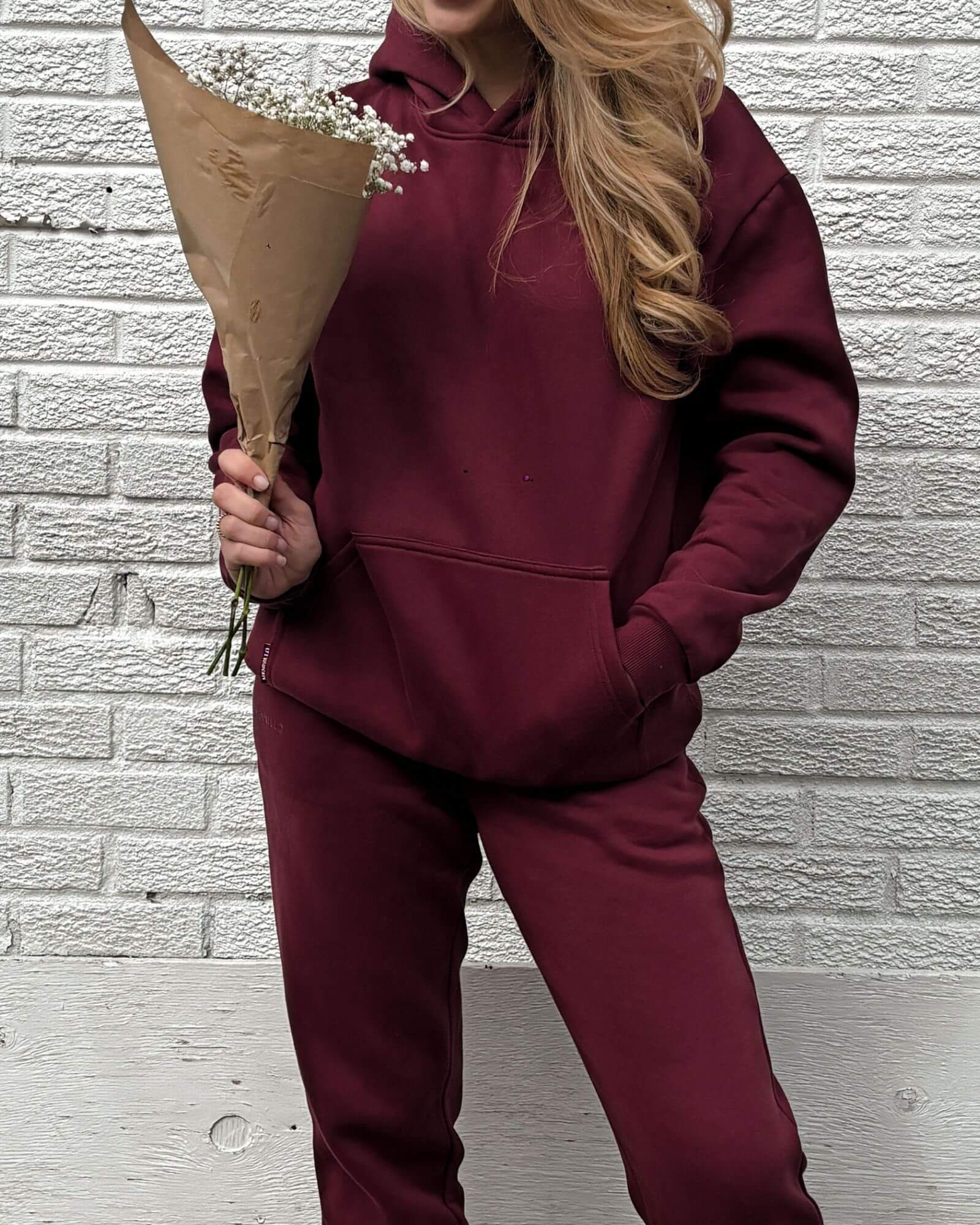 Front view of a girl holding a bouquet of flowers in front of a white brick wall wearing a cute burgundy matching set.