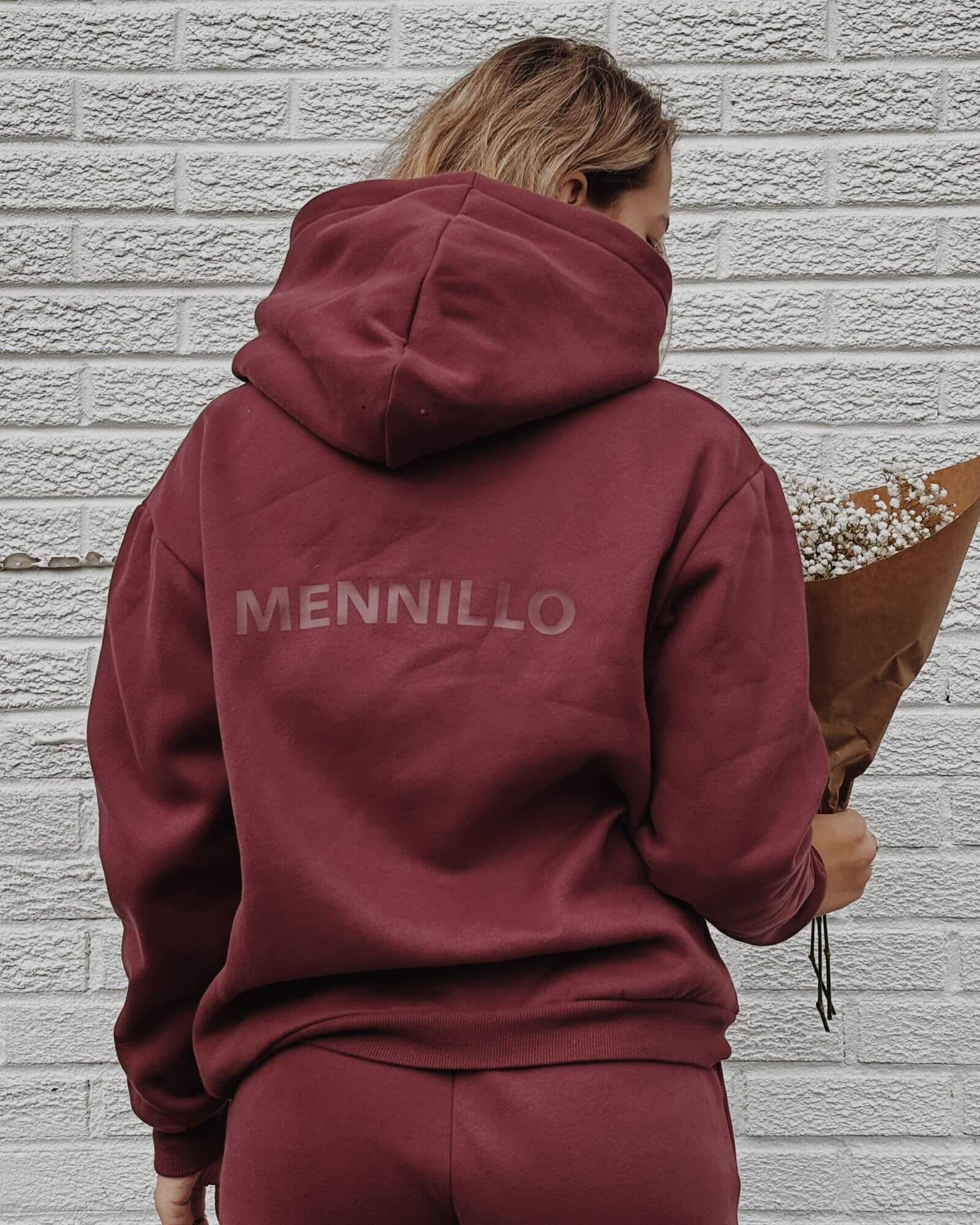 Back view of a girl holding a bouquet of flowers in front of a white brick wall wearing a cute burgundy matching set.