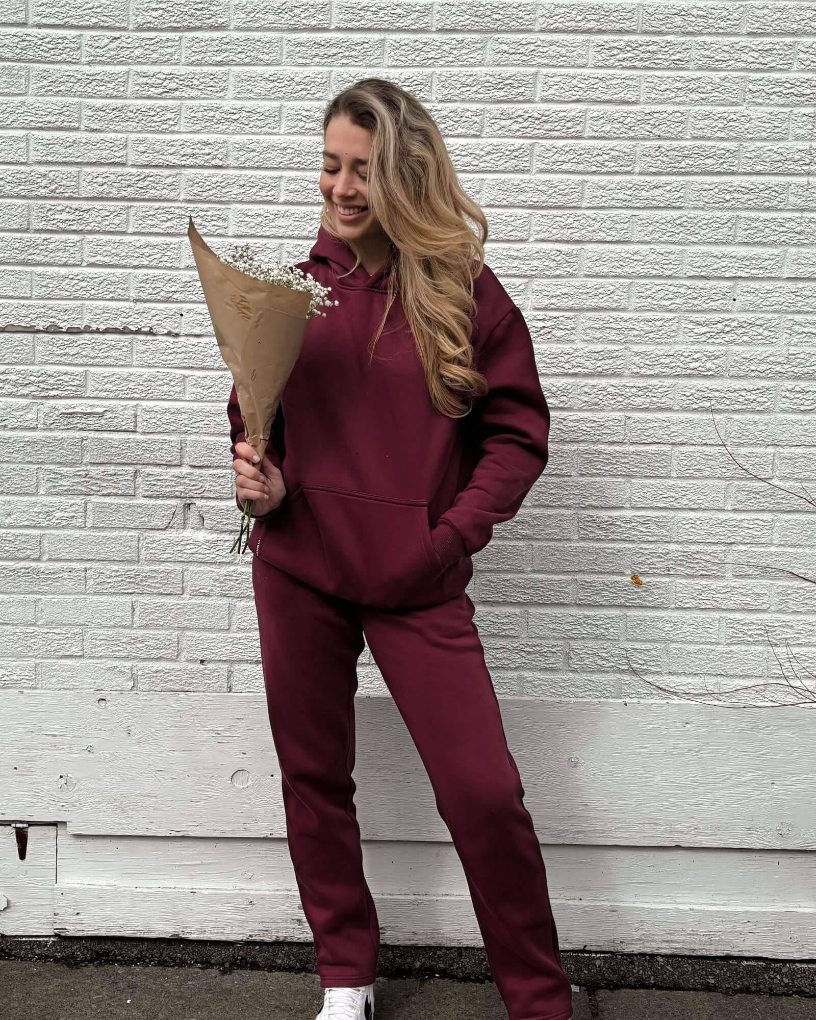 Pretty girl holding a bouquet of flowers in front of a white brick wall in her cute burgundy matching set.