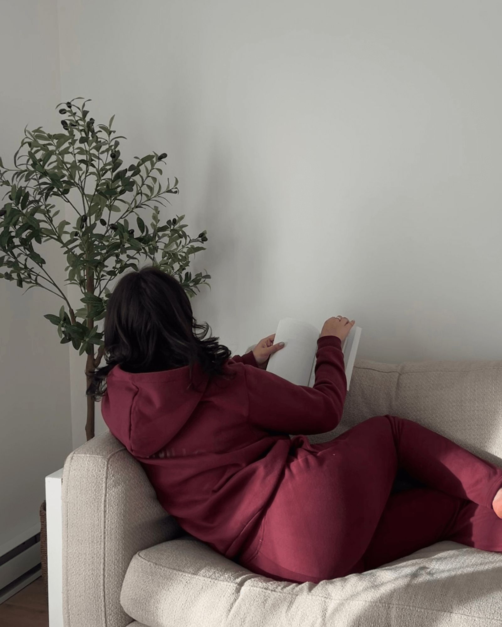 Brunette girl is sitting on a couch while reading a book in her cute burgundy matching set.