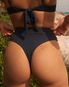 Close-up of a girl near the beach wearing a cute marine rib bikini bottom with her hands on her hips.