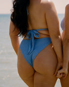 Close-up of a pretty girl wearing a cute blue crinkle bikini in front of the ocean.