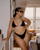 Pretty brunette girl is posing in a beach house while wearing her cute black rib bikini and black sunglasses.