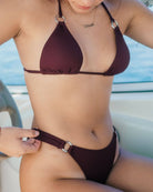 Beautiful girl is sitting on a boat while wearing a cute burgundy rib bikini.