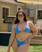 Pretty girl posing in a backyard with one hand on her hip wearing a cute blue crinkle bikini.