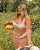 Pretty girl is holding a basket of lemons and taking a glass of white wine while wearing a cute floral pink bikini.