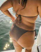 A girl is standing on a boat in the water while wearing a cute brown rib bikini.