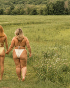 Two pretty girls are walking in a field while holding hands wearing cute bikinis.