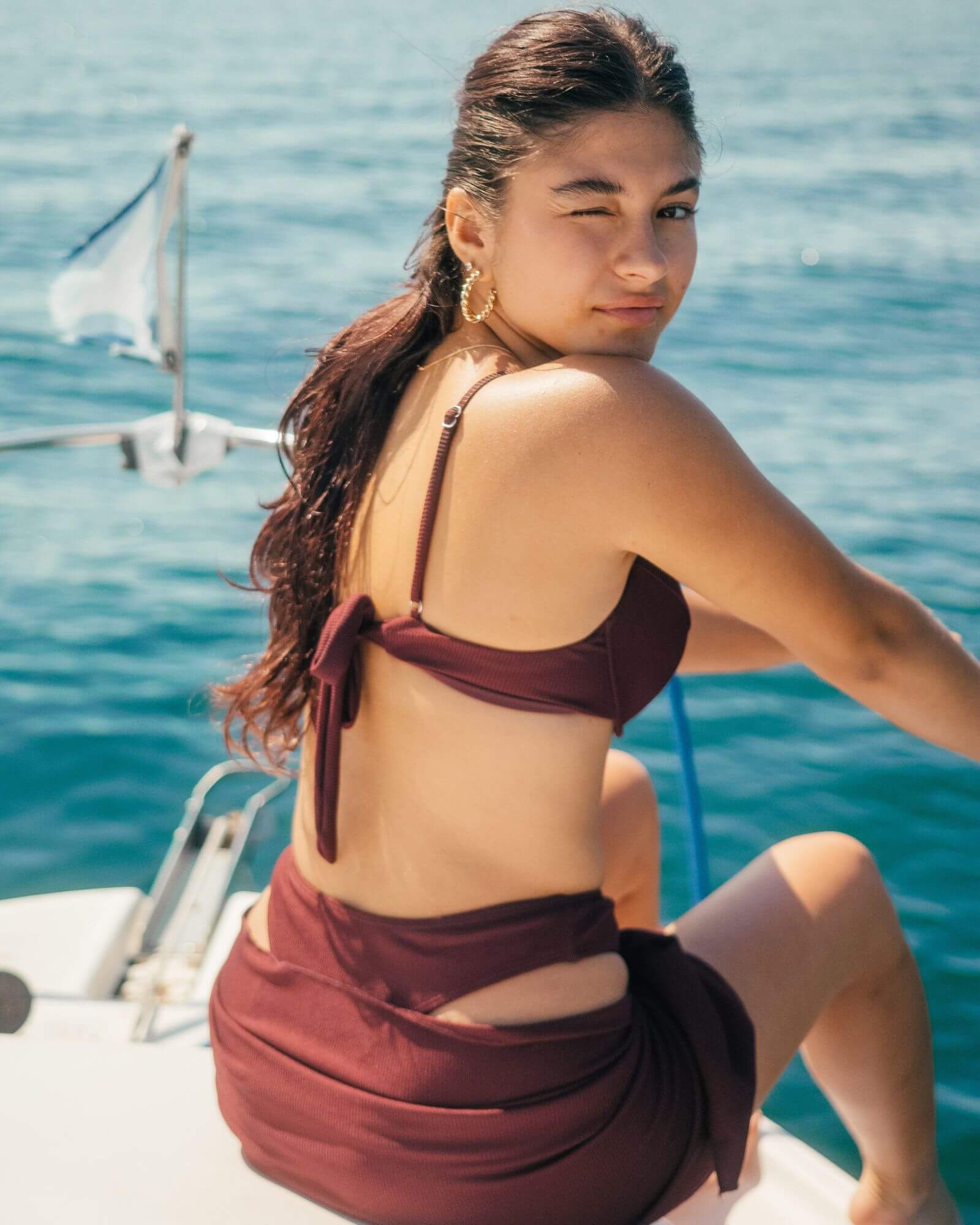 Beautiful girl sitting on a boat while wearing a cute burgundy rib bikini along with the matching sarong.