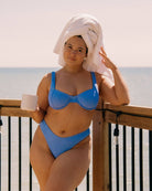 Pretty girl is standing with a towel on her head in her cute blue crinkle bikini with a mug in her hand.